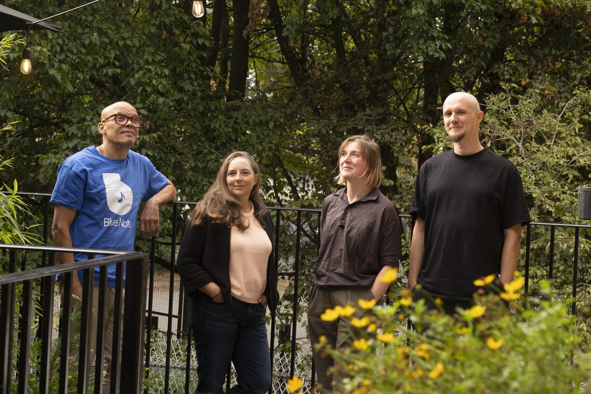 Four members of the CrossSense team standing together on a leafy terrace beside yellow flowers.